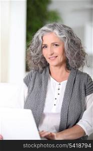 Grey-haired woman sat using laptop at home