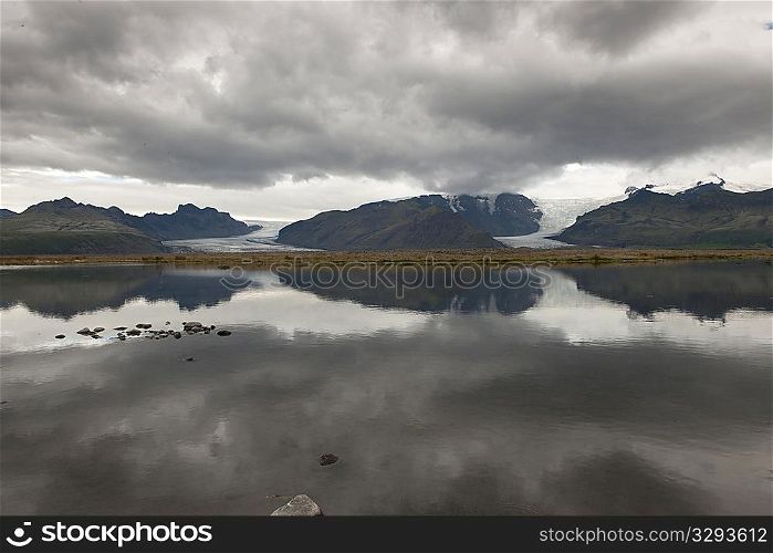 Grey mountains glaciers and dark clouds reflected in the lake