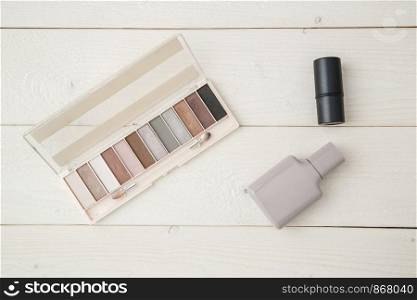 grey perfume bottle,highlighter and eye shadow on light wooden background. flat lay