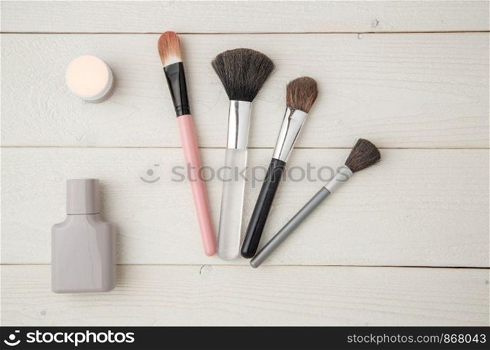 grey perfume bottle,highlighter,eye shadow and brush on light wooden background. flat lay