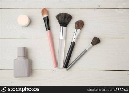grey perfume bottle,highlighter,eye shadow and brush on light wooden background. flat lay