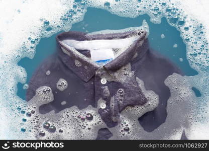 Grey polo shirt soak in powder detergent water dissolution, washing cloth. Laundry concept