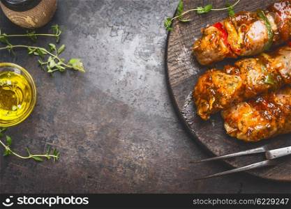 Grill food background with marinated skewers, meat fork, herbs spices and oil on dark rust metal background, top view, place for text, horizontal
