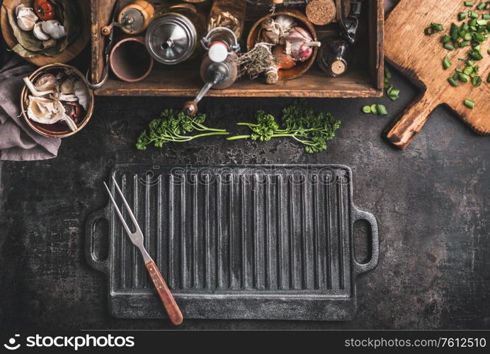 Grill or BBQ food background with empty cast iron grill griddle and meat fork on roast rustic kitchen table. Wooden box with seasonings, oils and other kitchen utensils.Top view. Place for design