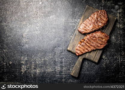 Grill steak on a wooden cutting board. On a black background. High quality photo. Grill steak on a wooden cutting board.