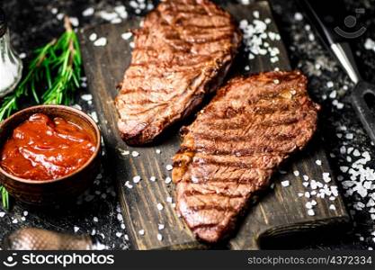 Grill steak on a wooden cutting board. On a black background. High quality photo. Grill steak on a wooden cutting board.