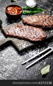 Grill steak on a wooden cutting board. On a black background. High quality photo. Grill steak on a wooden cutting board.