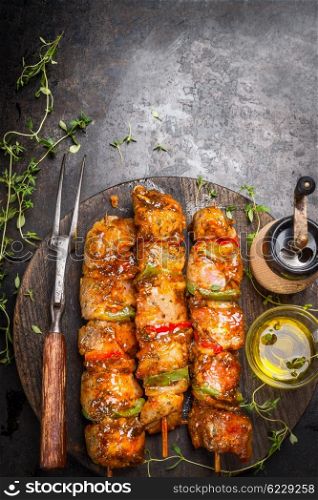 Grill time with marinated skewers, meat fork, herbs spices and oil on dark rust metal background, top view, place for text