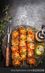 Grill time with marinated skewers, meat fork, herbs spices and oil on dark rust metal background, top view, place for text