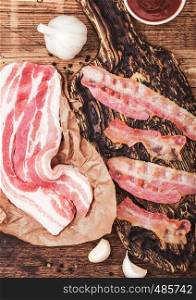 Grilled bacon strips on vintage wooden board with raw fresh smoked pork bacon on butchers paper with meat hatchet on wood board.