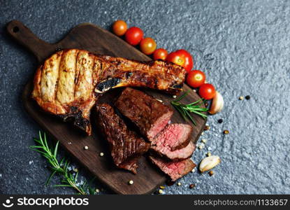 Grilled beef meat slice on black background / Roasted beef steak fillet and pork chops with herb and spices serve with vegetable on wooden cutting board