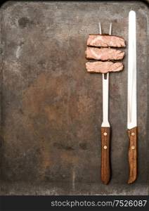 Grilled beef meat with fork and knife on metal kitchen desk. Food background