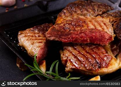 Grilled beef steak. Grilled cut of beef steak in pan with spices on dark stone background