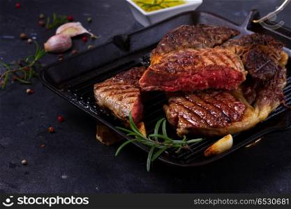 Grilled beef steak. Grilled juisy beef steak in pan with spices on dark stone background