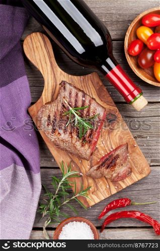 Grilled beef steak with rosemary, salt and pepper and wine bottle on wooden table. Top view
