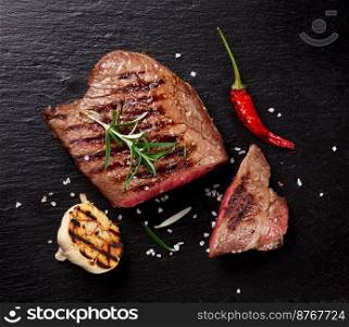 Grilled beef steak with rosemary, salt and pepper on black stone plate. Top view