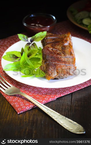 Grilled beef steak with salad and souce on wooden table. Grilled beef steak with salad and souce on wooden table at white plate. Salad with tomatoes and cucumbers and souce barbecue. Leafs of basil as decoration.