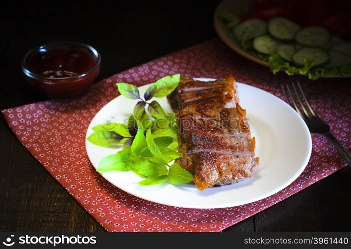 Grilled beef steak with salad and souce on wooden table. Grilled beef steak with salad and souce on wooden table at white plate. Salad with tomatoes and cucumbers and souce barbecue. Leafs of basil as decoration.