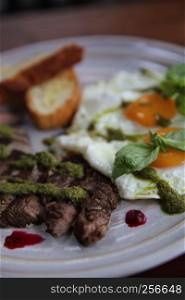 Grilled beef steak with toast , fried egg and vegetables on top with pesto sauce