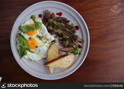 Grilled beef steak with toast , fried egg and vegetables on top with pesto sauce