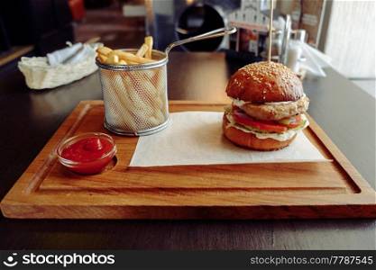 Grilled burger and french fries on wooden board with tomato sause. Tasty grilled burger and french fries