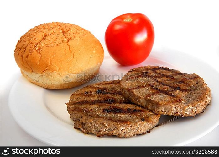 Grilled burger patties with a tomato and a bun