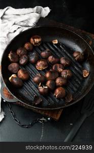 Grilled chestnuts in a frying pan on a dark background