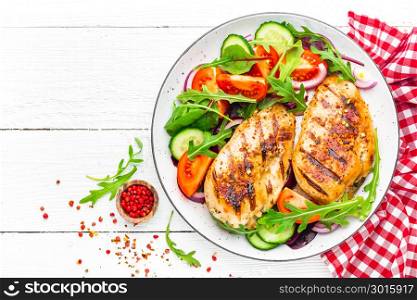 Grilled chicken breast. Fried chicken fillet and fresh vegetable salad of tomatoes, cucumbers and arugula leaves. Chicken meat salad. Healthy food. Flat lay. Top view. White background