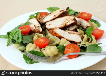 Grilled chicken breast slices served on a bed of pasta shells, garnished with tomato and fresh basil