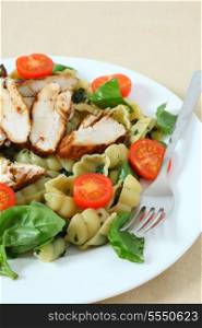 Grilled chicken breast slices served on a bed of pasta shells, garnished with tomato and fresh basil