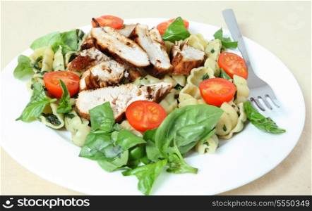 Grilled chicken breast slices served on a bed of pasta shells with spinach, garnished with tomato and fresh basil