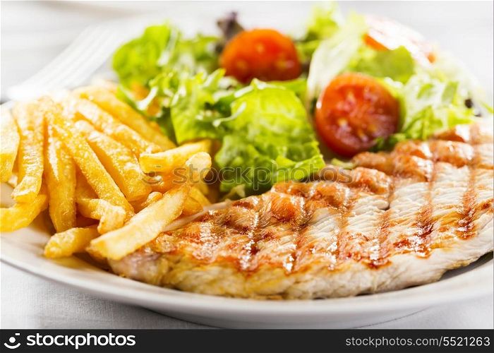 Grilled chicken breast with fries and salad