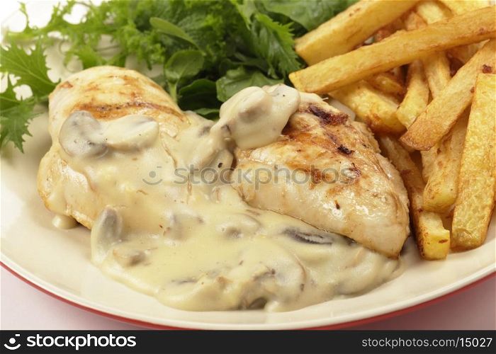 Grilled chicken breasts closeup topped with a creamy mushroom sauce and served with french fried potato chips and a garden fresh green salad.