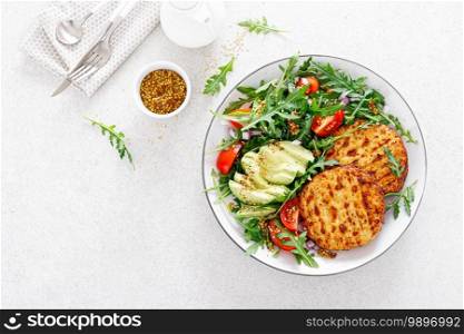 Grilled chicken burgers, avocado and fresh vegetable salad with tomato and arugula, top view