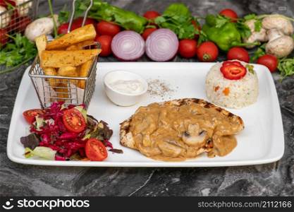 Grilled chicken in mushroom sauce with french fries and salad on marble table
