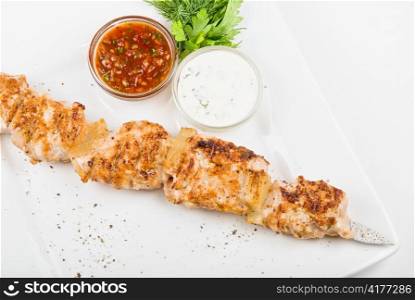 Grilled chicken kebab with sauce and greens on white plate