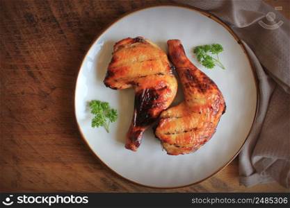 Grilled chicken leg quarters with crispy golden brown skin, lemon, parsley on white plate on dark wooden boards. Food background. Top view .. Grilled chicken leg quarters with crispy golden brown skin, lemon, parsley on white plate on dark wooden boards. Food background. Top view