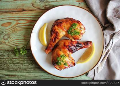 Grilled chicken leg quarters with crispy golden brown skin, lemon, parsley on white plate on dark wooden boards. Food background. Top view .. Grilled chicken leg quarters with crispy golden brown skin, lemon, parsley on white plate on dark wooden boards. Food background. Top view