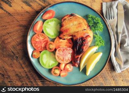Grilled chicken leg quarters with crispy golden brown skin, tomatoe ,lemon on dark wooden boards. Food background. Top view