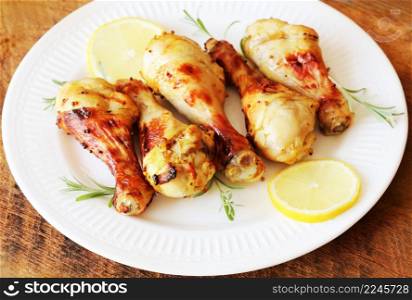 Grilled chicken legs with mustard on wooden table served on white plate with rosemary and lemon. BBQ dinner background .. Grilled chicken legs with mustard on wooden table served on white plate with rosemary and lemon. BBQ dinner background