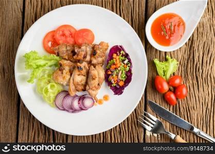 Grilled chicken on a white plate with a salad, tomatoes, chilies cut into pieces and sauce on wooden table. Top view.