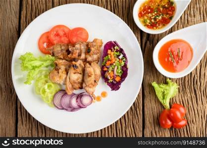 Grilled chicken on a white plate with a salad, tomatoes, chilies cut into pieces and sauce on wooden table. Top view.