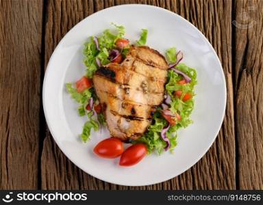 Grilled chicken on a white plate with a salad, tomatoes, chilies cut into pieces on wooden table.Top view.