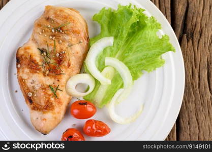 Grilled chicken on a white plate with tomatoes, salad and onion.