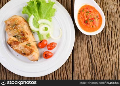 Grilled chicken on a white plate with tomatoes, salad, onion and chili sauce.