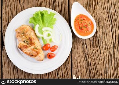 Grilled chicken on a white plate with tomatoes, salad, onion and chili sauce.