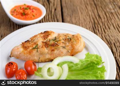 Grilled chicken on a white plate with tomatoes, salad, onion and chili sauce.
