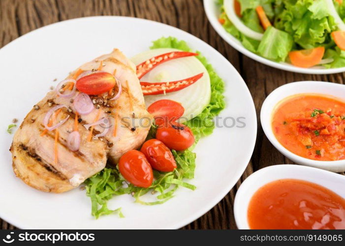 Grilled chicken on a white plate with tomatoes, salad, onion, chili and sauce.