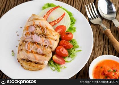 Grilled chicken on a white plate with tomatoes, salad, onion, chili and sauce.