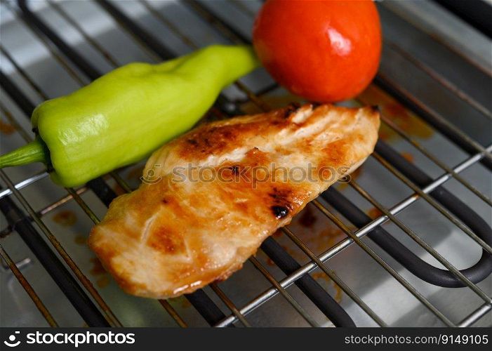 Grilled chicken on an electric grill with paprika and tomato.
